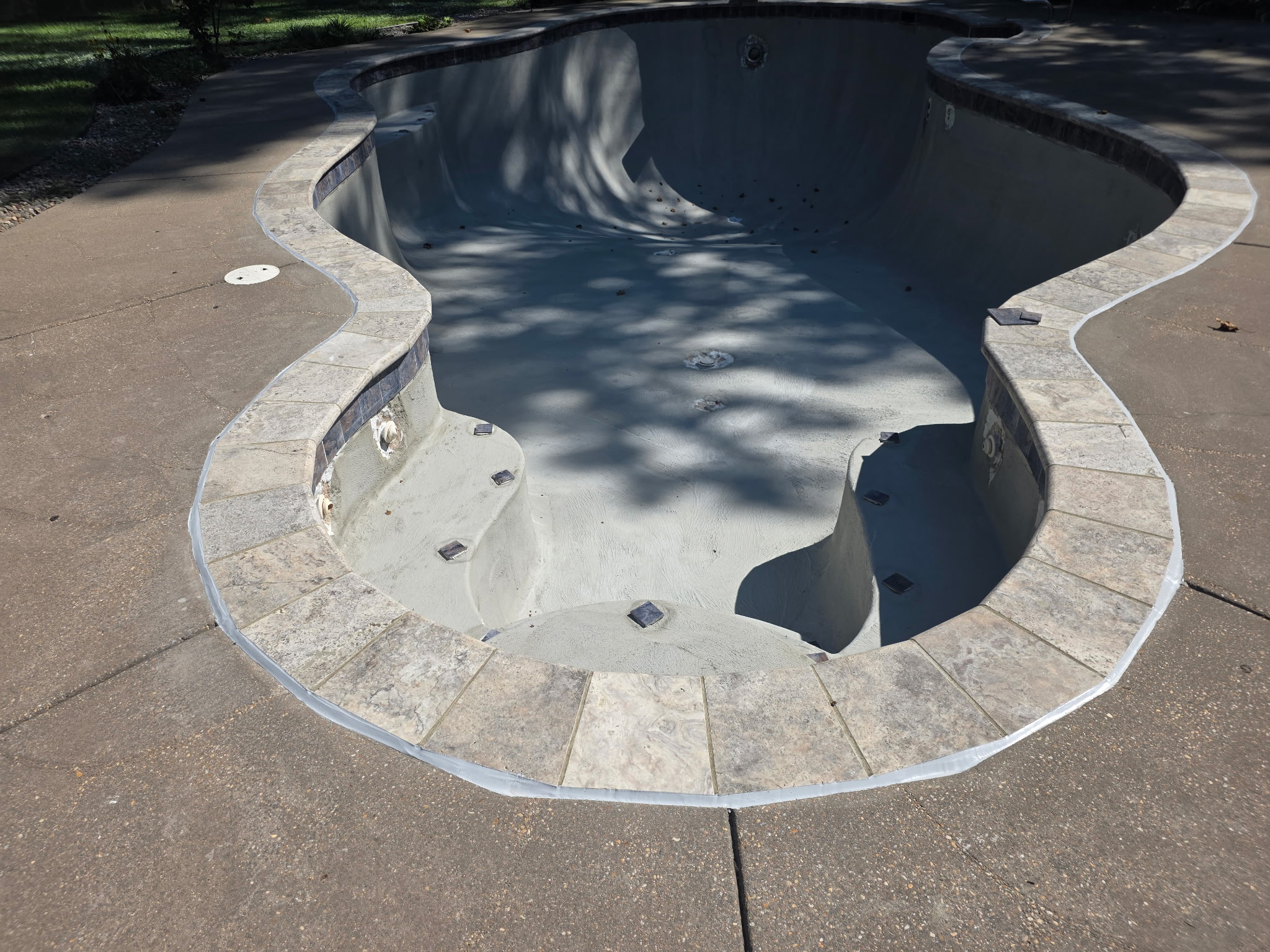 Freeform pool drained during an AquaPros renovation — freshly applied plaster, new waterline tile, travertine coping and mosaic step markers