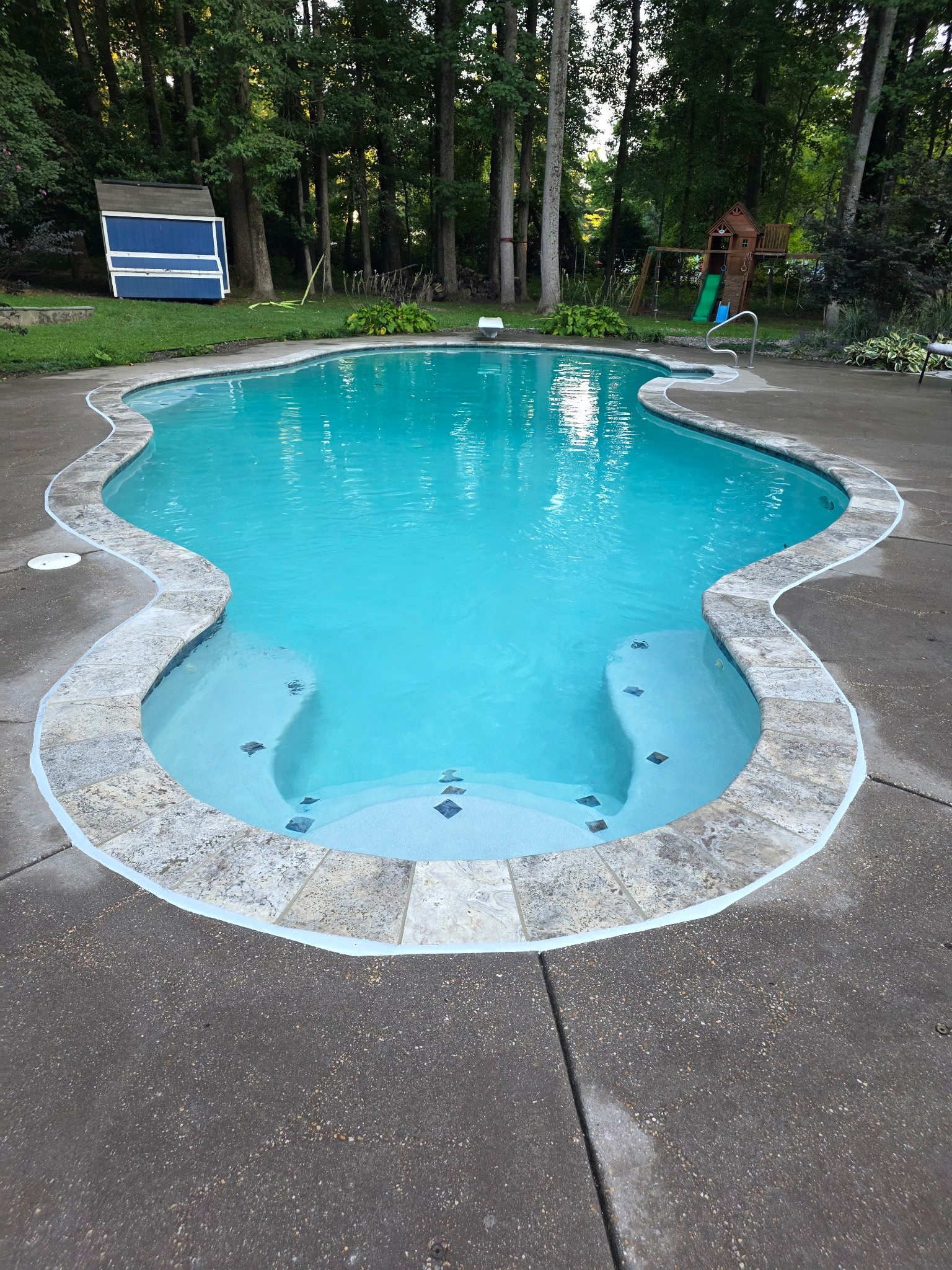 The same freeform pool after the AquaPros renovation — filled with clear blue water over the new plaster, tile and travertine coping